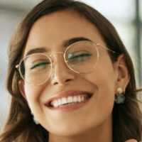 Cheerful business woman with glasses posing with her hands under her face showing her smile in an office. Playful hispanic female entrepreneur looking happy and excited at workplace